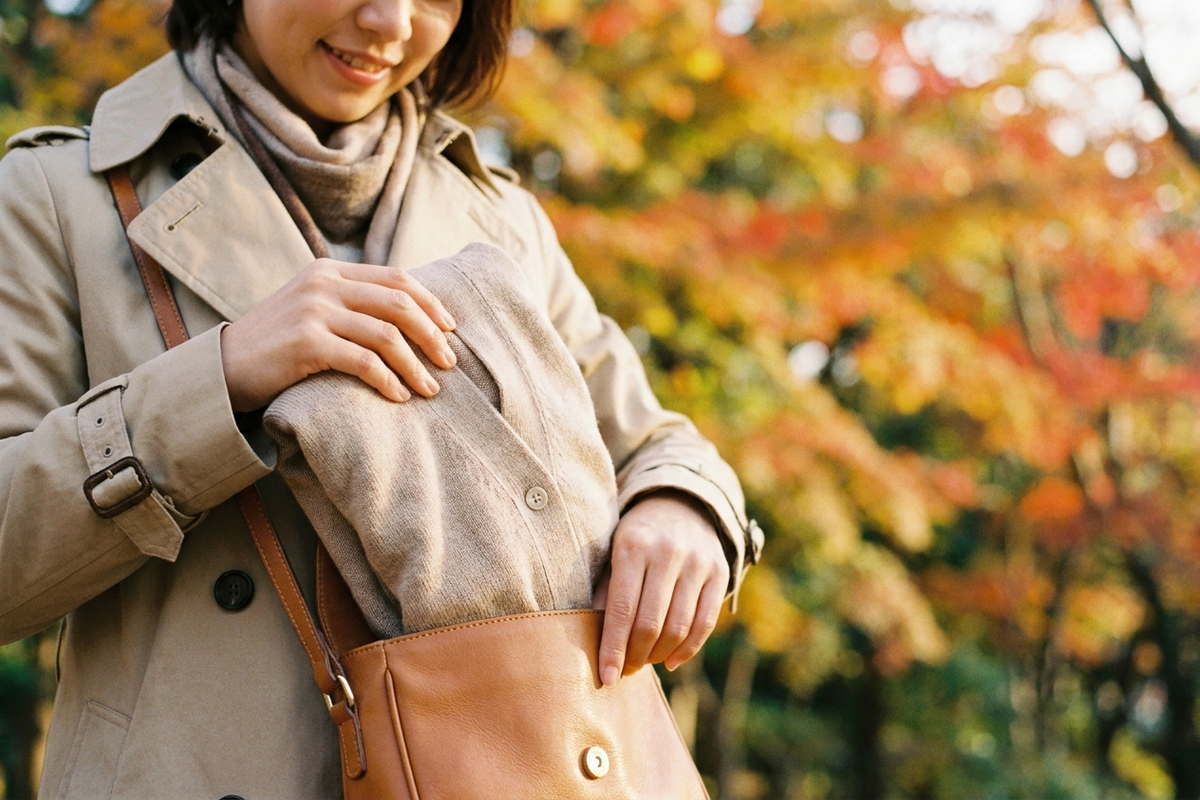 小さめバッグに羽織りを畳んで入れる準備をする女性
