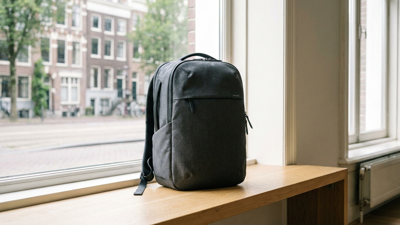 Mochila técnica para portátil de color gris oscuro apoyada sobre un banco de madera clara en un espacio urbano luminoso, sin personas ni texto
