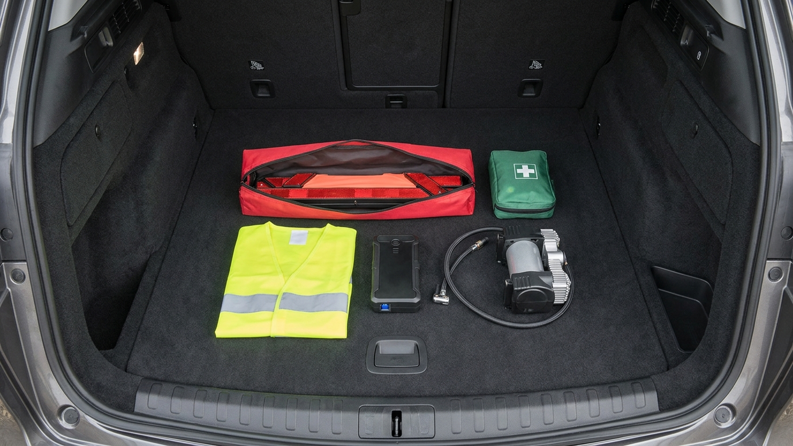 Bagagliaio di un'auto con kit di sicurezza, valigetta di pronto soccorso e accessori da viaggio ordinati per il rientro dalle vacanze